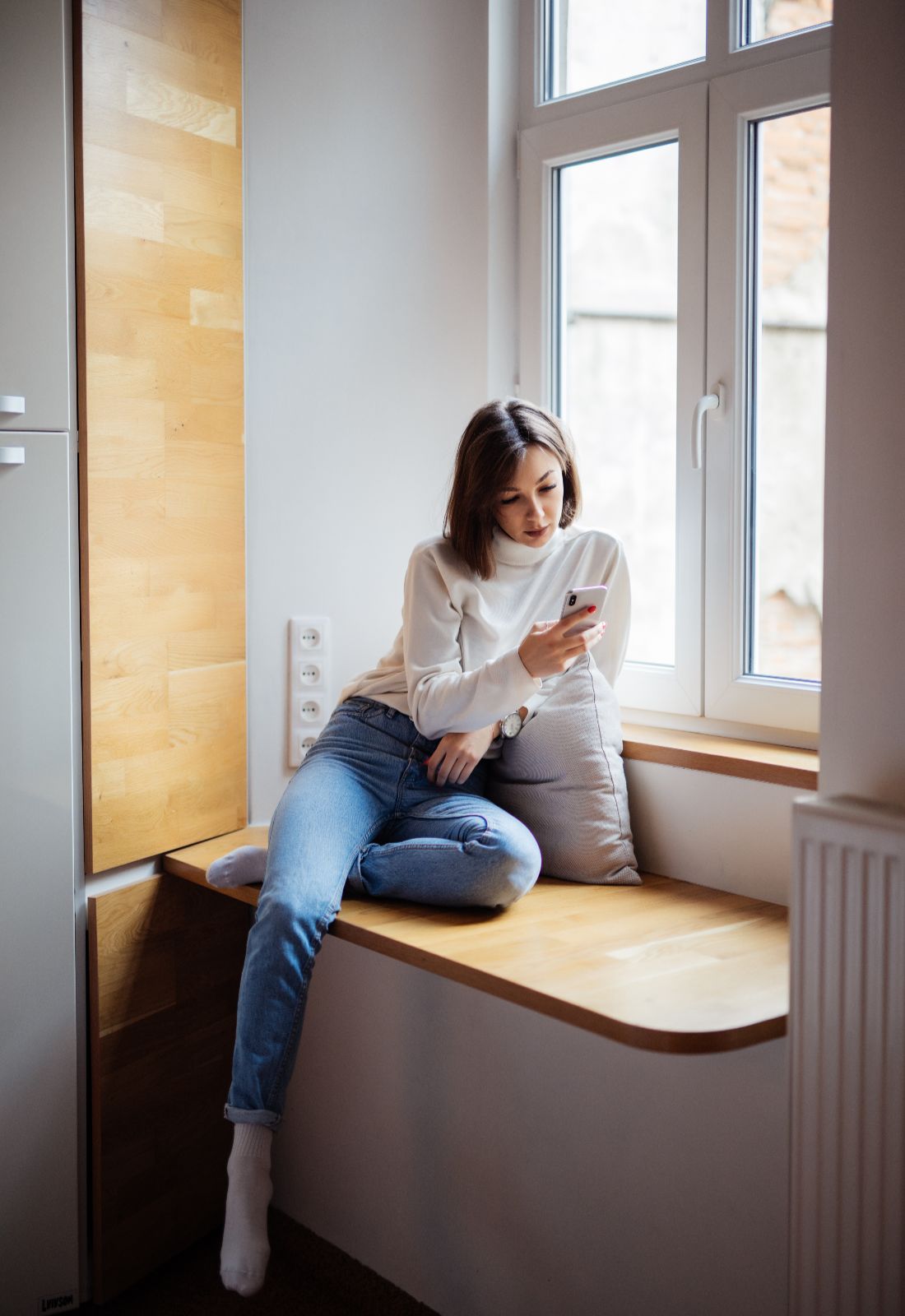 Beautiful young woman sitting wide windowhill blue jeans white t shirt (1)